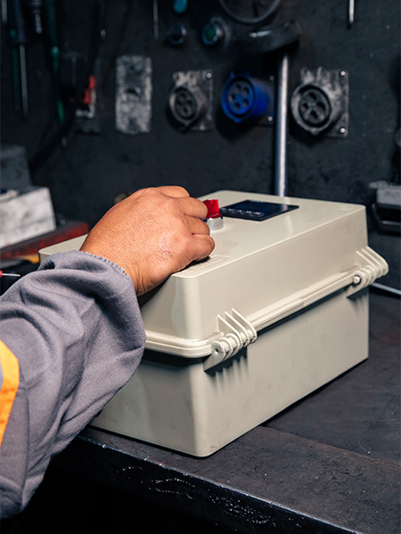 Mão de técnico acionando chave em caixa de controle elétrico portátil — manutenção elétrica industrial, diagnóstico de painéis