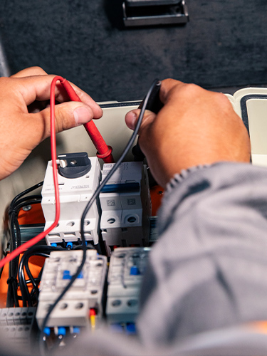 Técnico medindo e testando componentes dentro de painel elétrico com sondas e cabos — inspeção e montagem de painéis elétricos industriais
