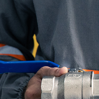 Mão de técnico segurando válvula metálica com haste azul